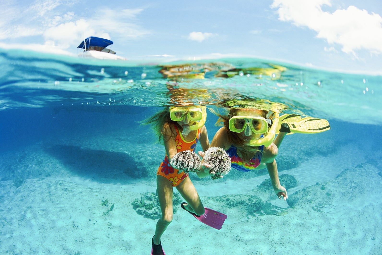 Cayman Islands, girls snorkeling holding sea urchins, boat above