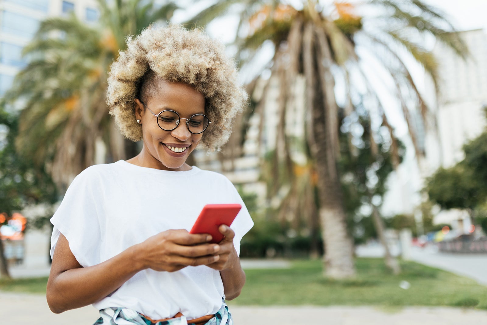 Woman smiling while using a mobile phone outdoors on the street.