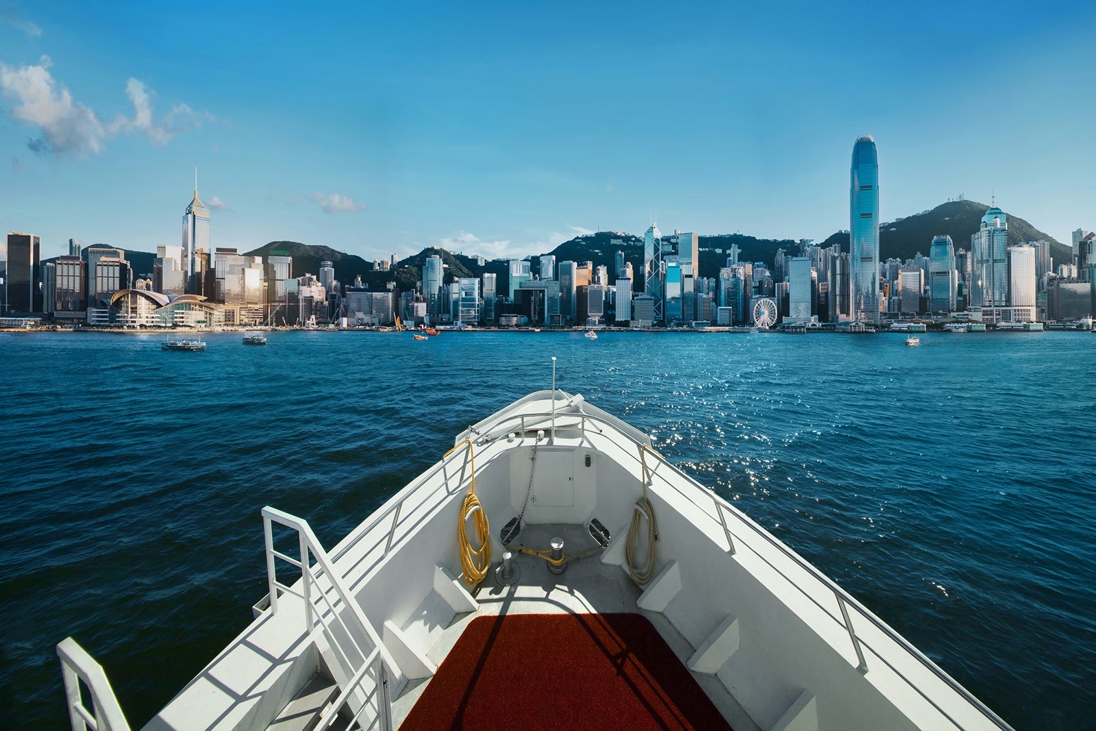 Cruise ship sailing across Victoria Harbour against the city skyline of Hong Kong on a sunny day