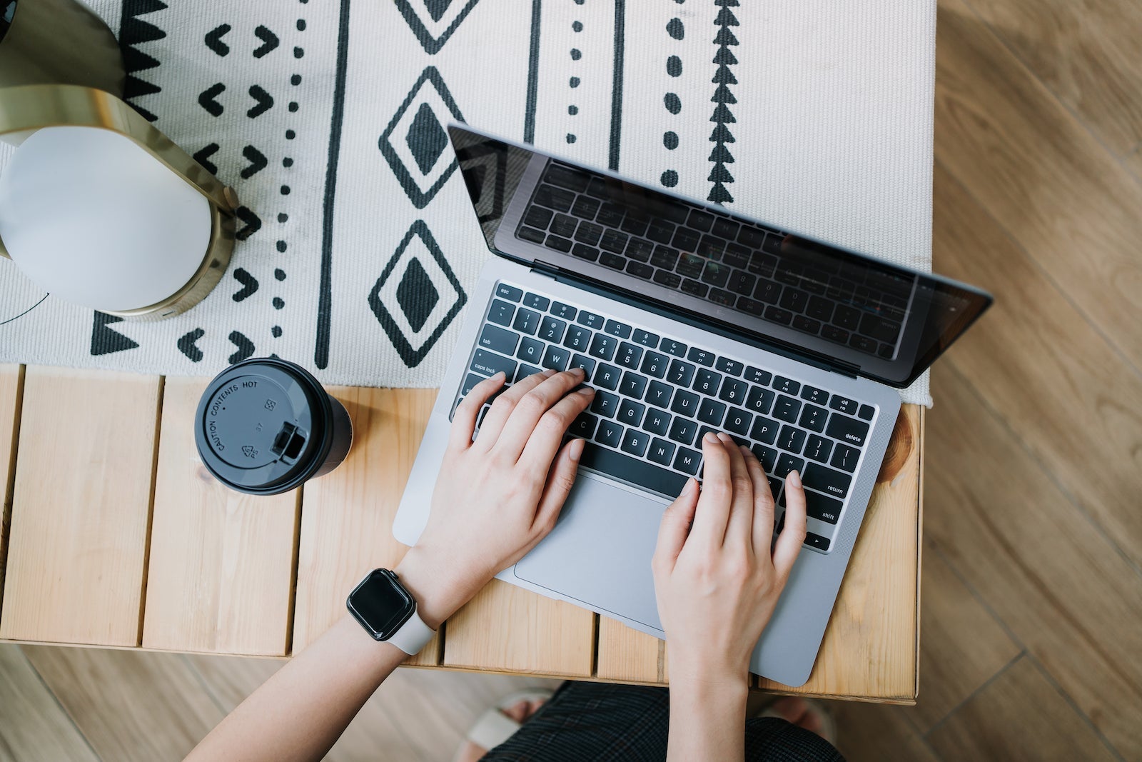 High angle view of woman using laptop on wooden desk, with a cup of coffee by her side. Lifestyle and technology. Staying connected throughout the city. Business on the go