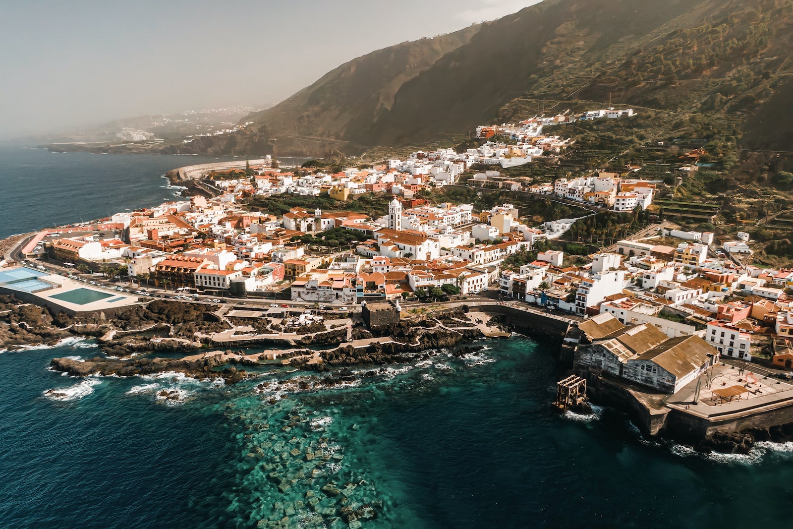 Aerial view of Garachico village on the coast of the Atlantic ocean in Tenerife island of Spain. Town on a rocky shore under the volcano mountain.