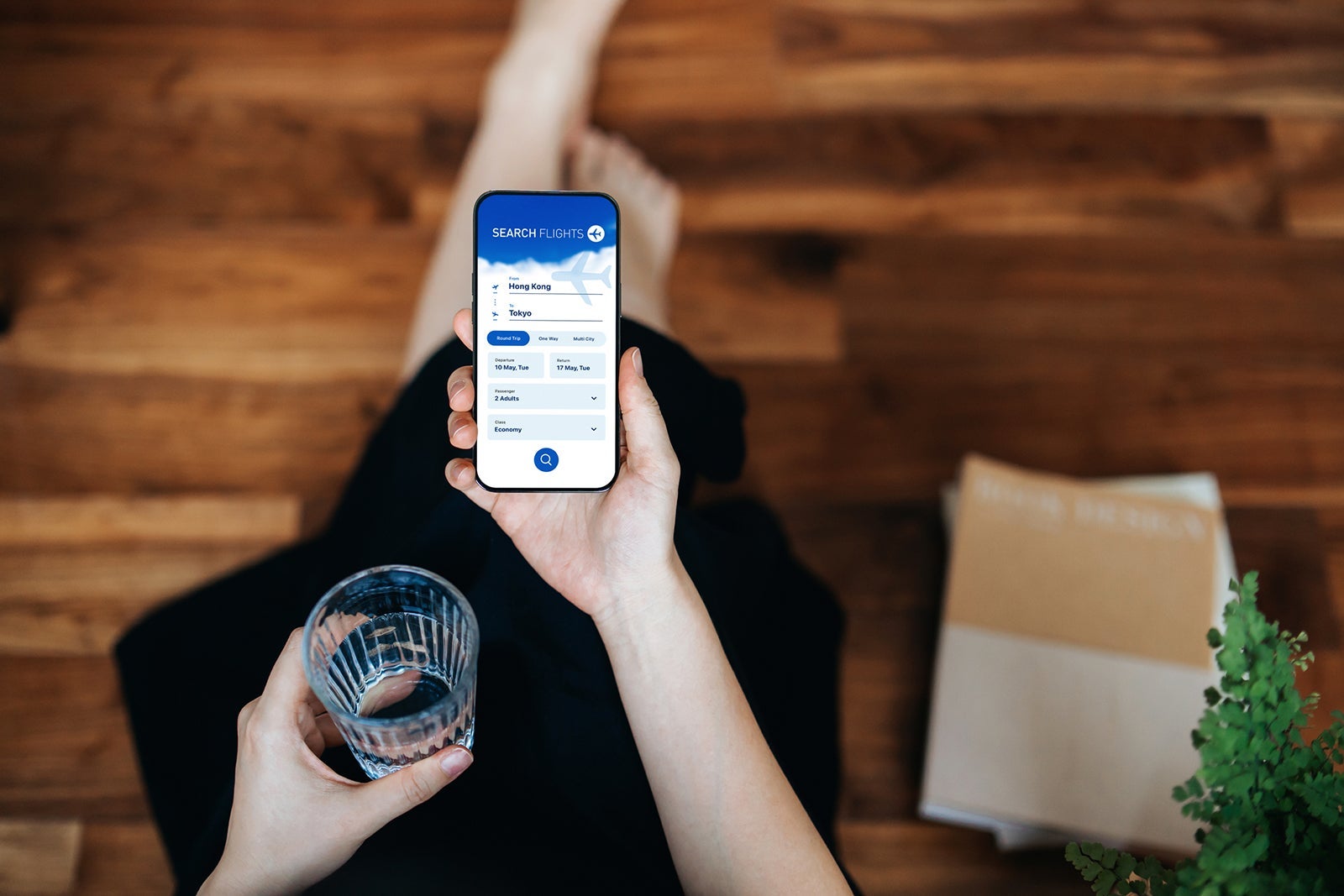 Overhead view of young Asian woman booking flight tickets on airline website online with smartphone at home. Travel planning. Booking a holiday online. Travel and vacations concept. Business person planning business trip