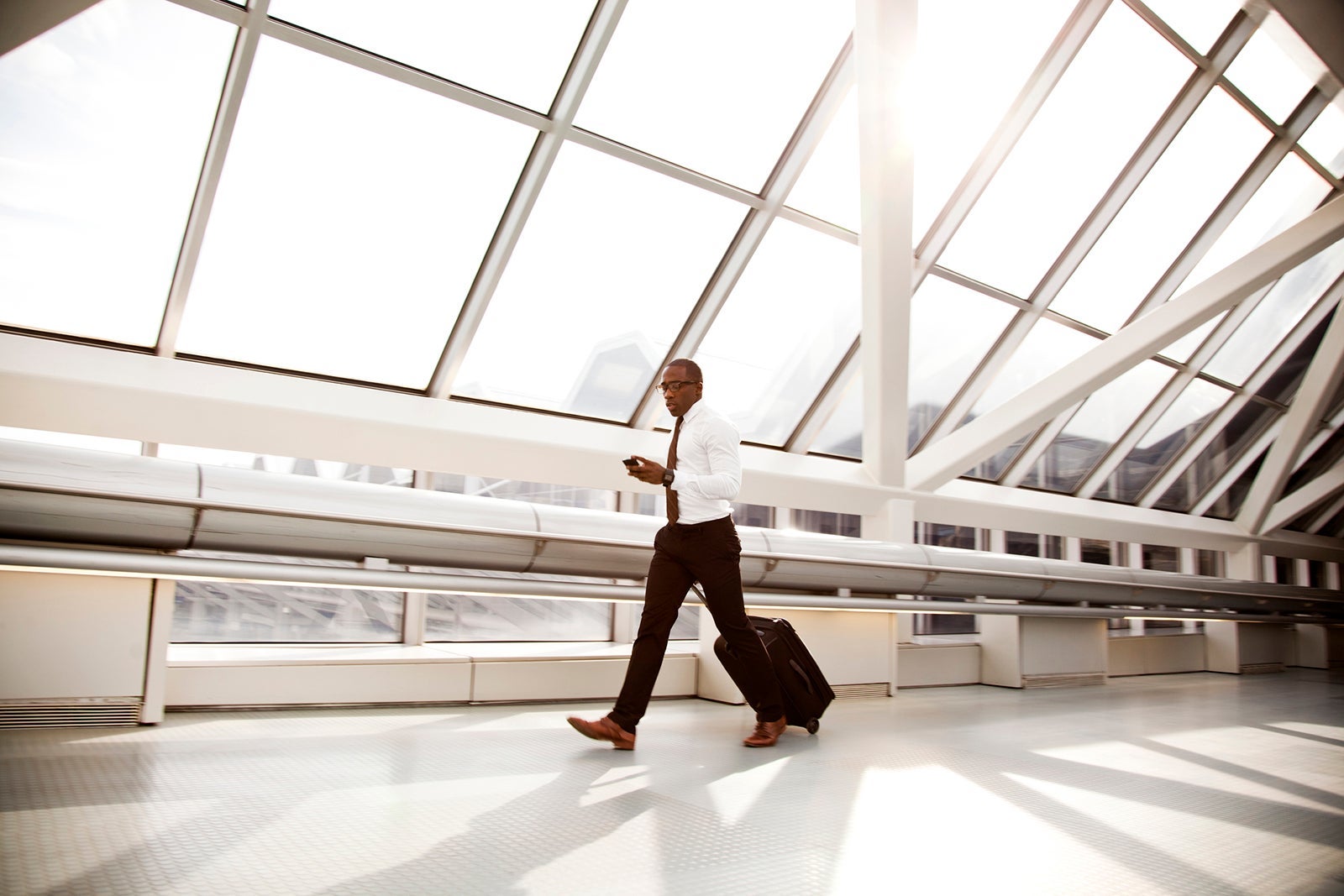 A well dressed businessman walking in an airport with a suitcase and a tablet device.
