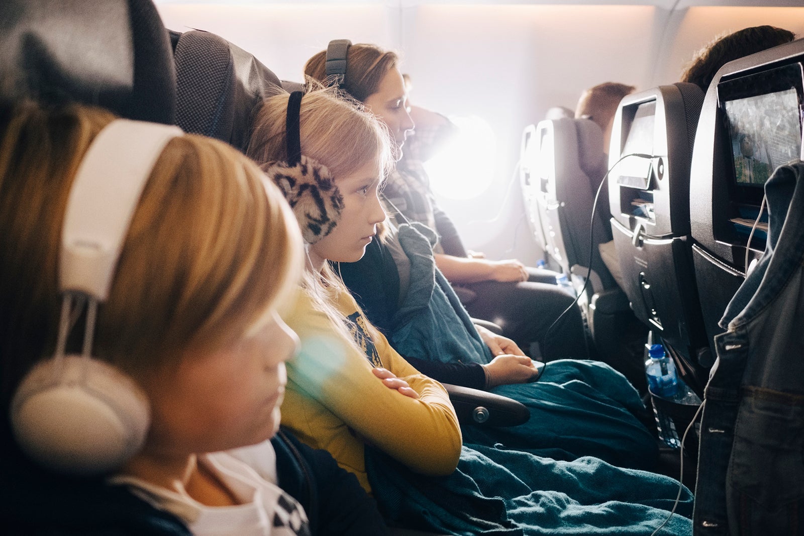Side view of mother and children sitting in airplane while using headphones