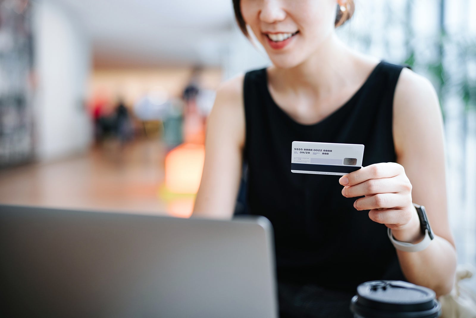 Cropped shot of smiling young Asian woman relaxing in cafe, shopping online using laptop and making mobile payment with credit card on hand. Lifestyle and technology. Comfortable and fast online shopping experience