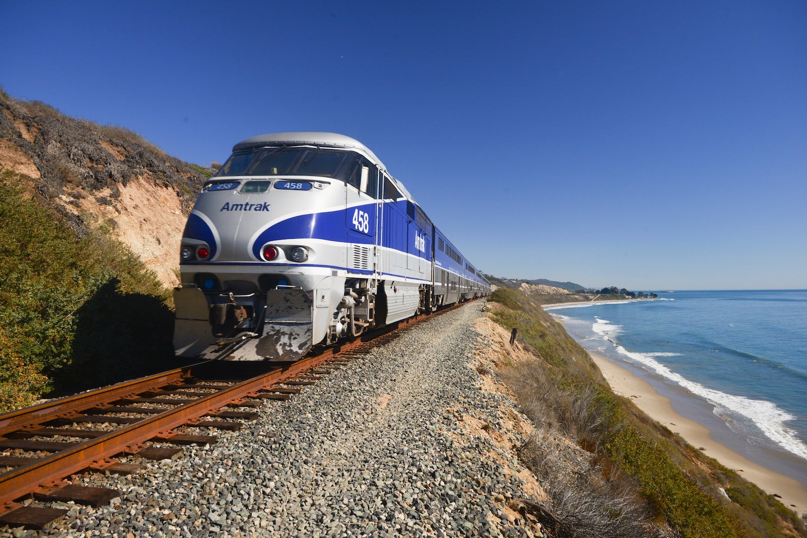 Amtrak Surfliner passenger train on tracks running alongside Pacific Ocean beaches near Santa Barbara on the west coast of California, USA