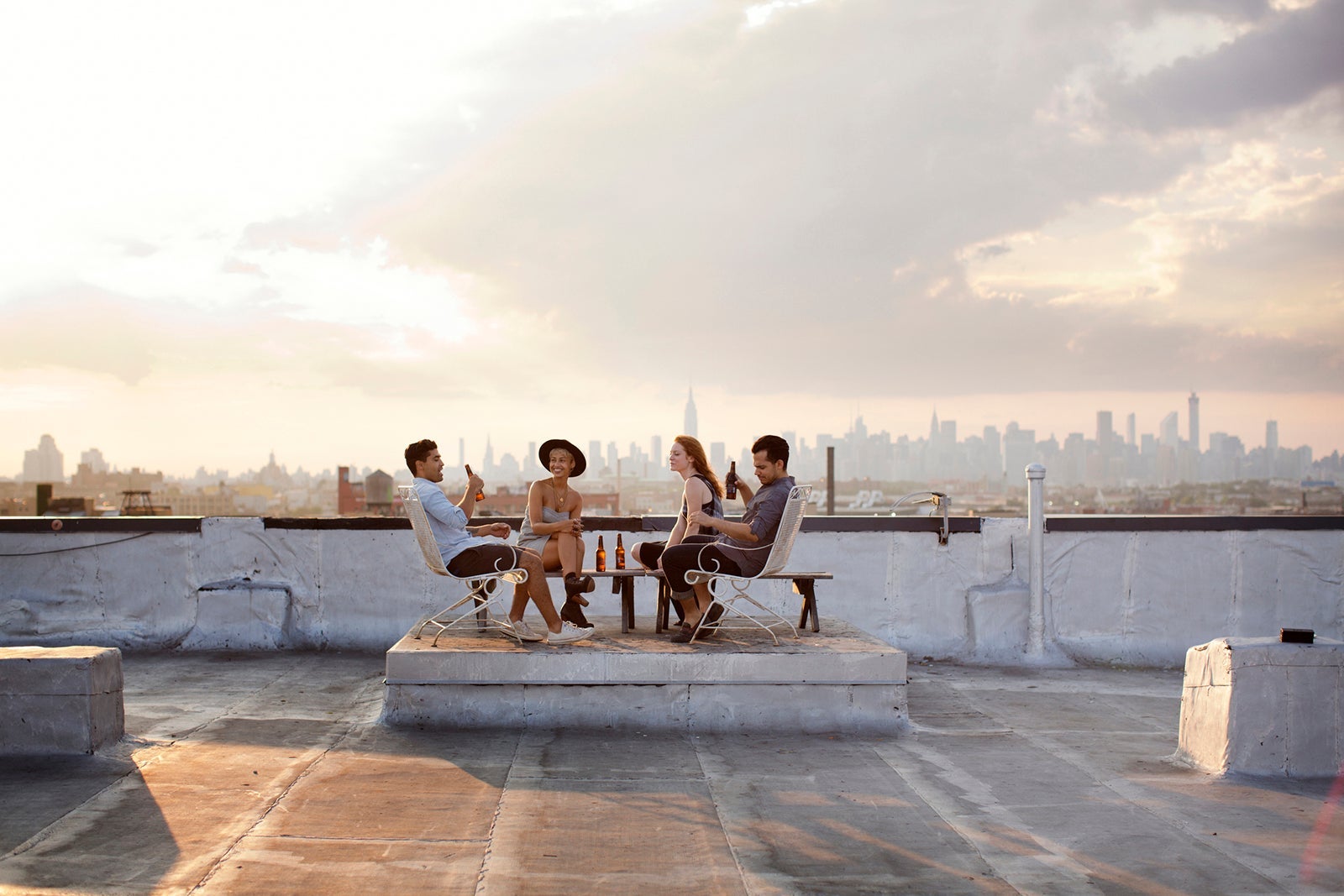 Happy friends enjoying while having beer at building terrace during sunset