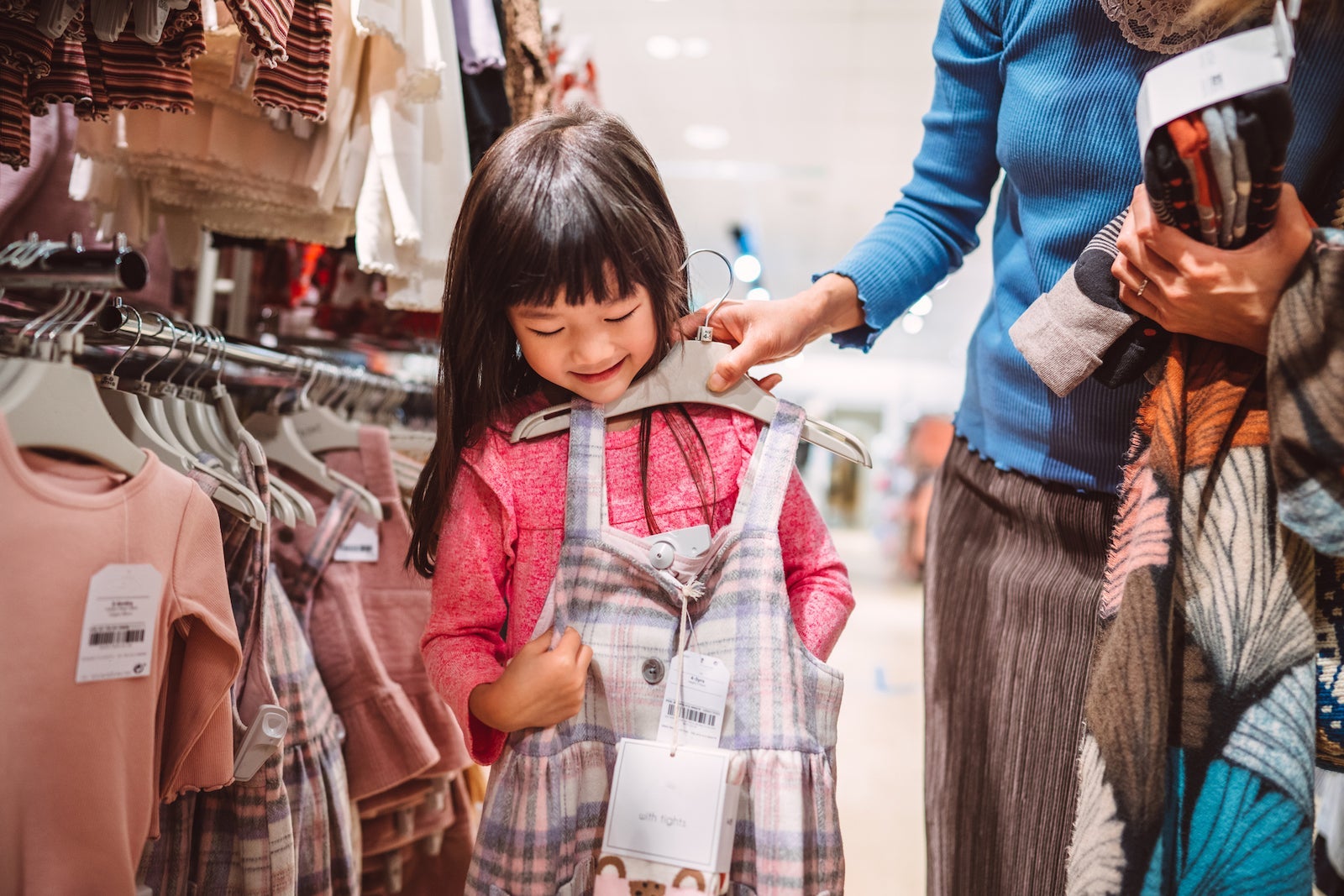 Mom fitting a dress on her lovely cheerful daughter in fashion boutique