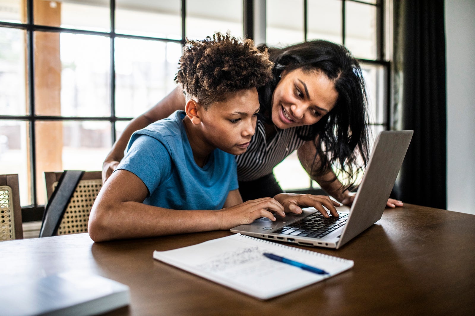 Mother helping teenage son with homework in residential kitchen
