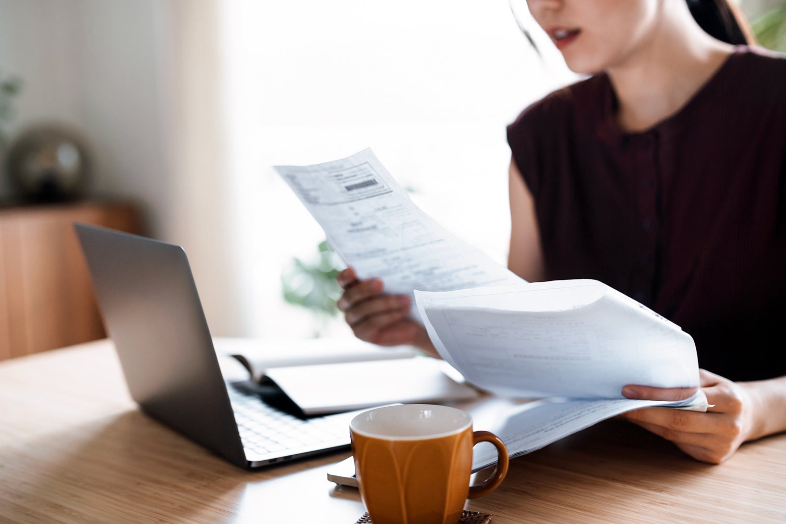 Cropped shot of Asian woman sitting at dining table, handling personal finance with laptop. She is making financial plan and planning budget as she go through her financial bills, tax and expenses at home. Wealth management, banking and finance concept