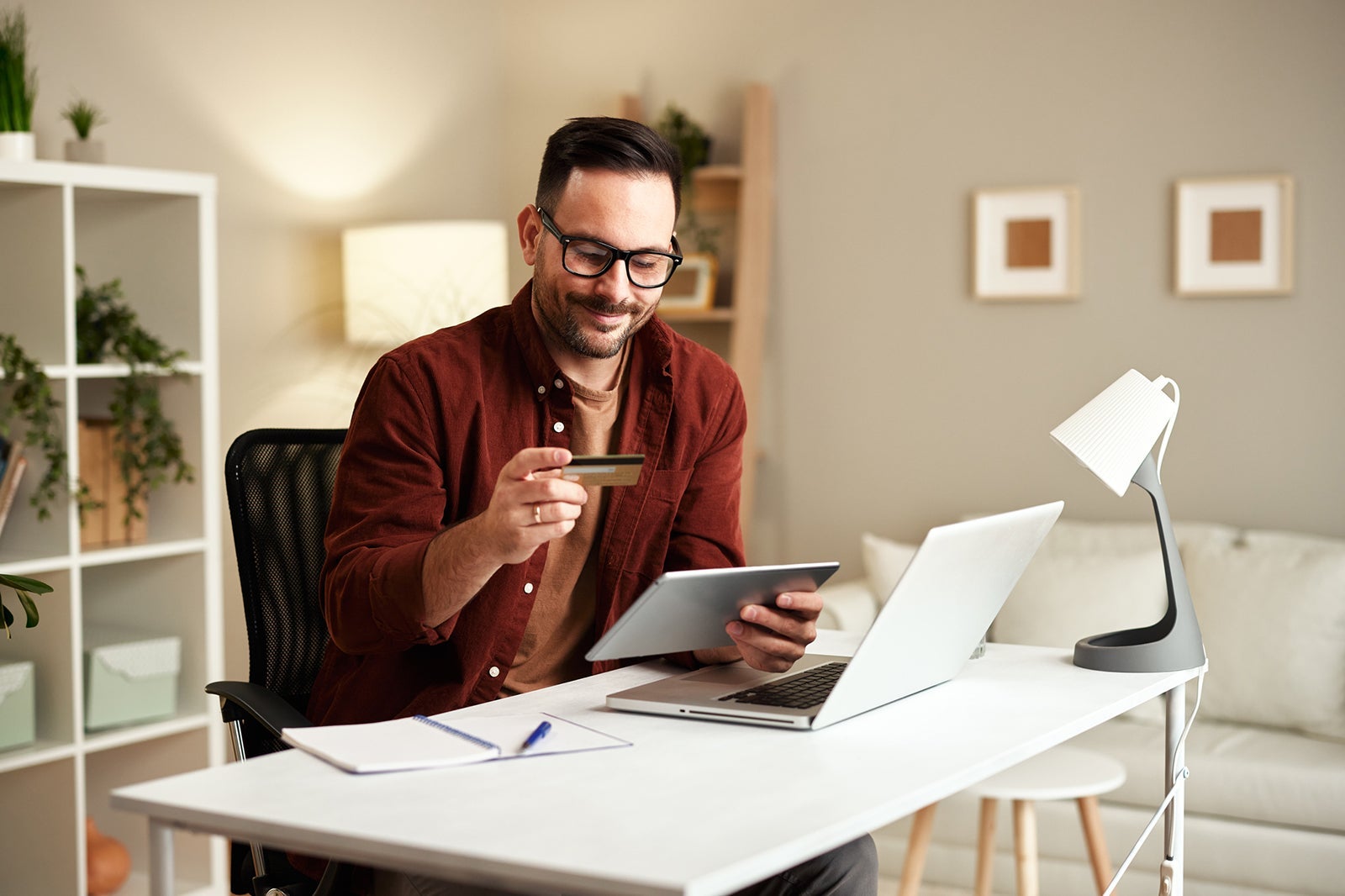 Young man holding credit card and tablet at home at table
