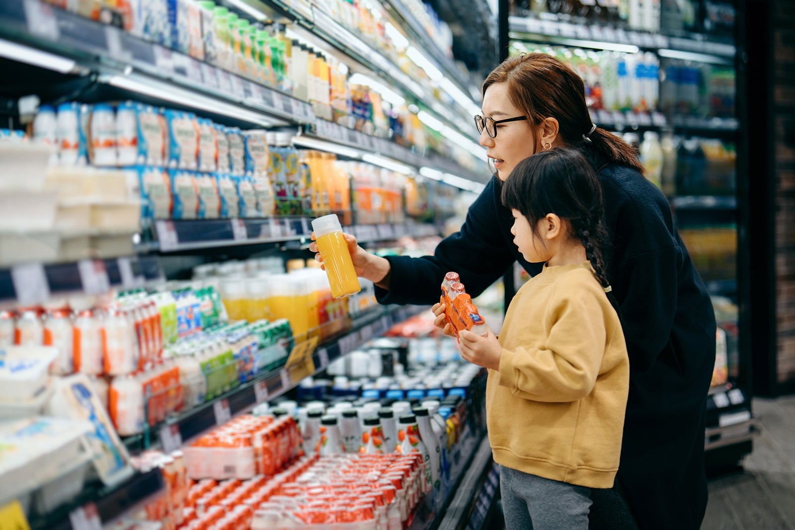 Young Asian mother and her little daughter grocery shopping in supermarket. they are choosing fresh fruit juice together along the beverage aisle. Routine grocery shopping. Healthy eating lifestyle