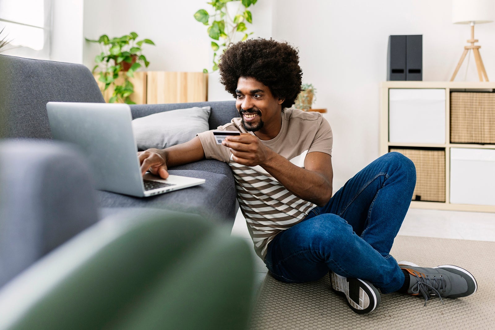 Happy young afro american man holding credit card while shopping online using laptop computer at home