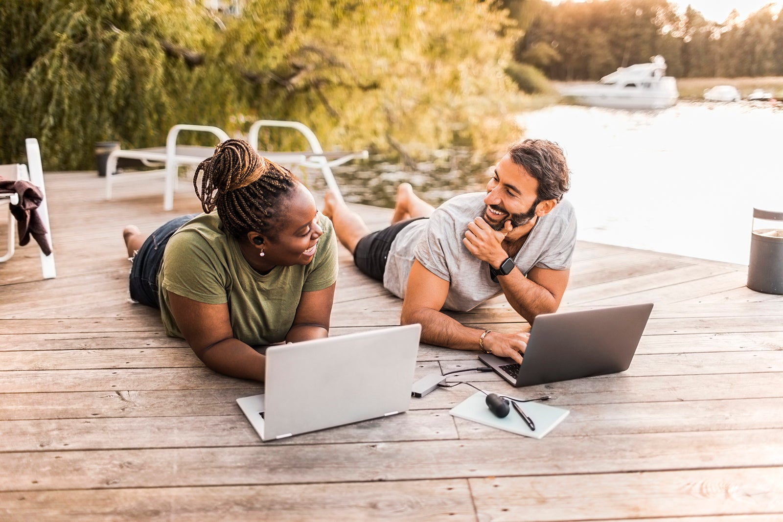 Smiling female and male colleagues working on laptop at jetty by sea