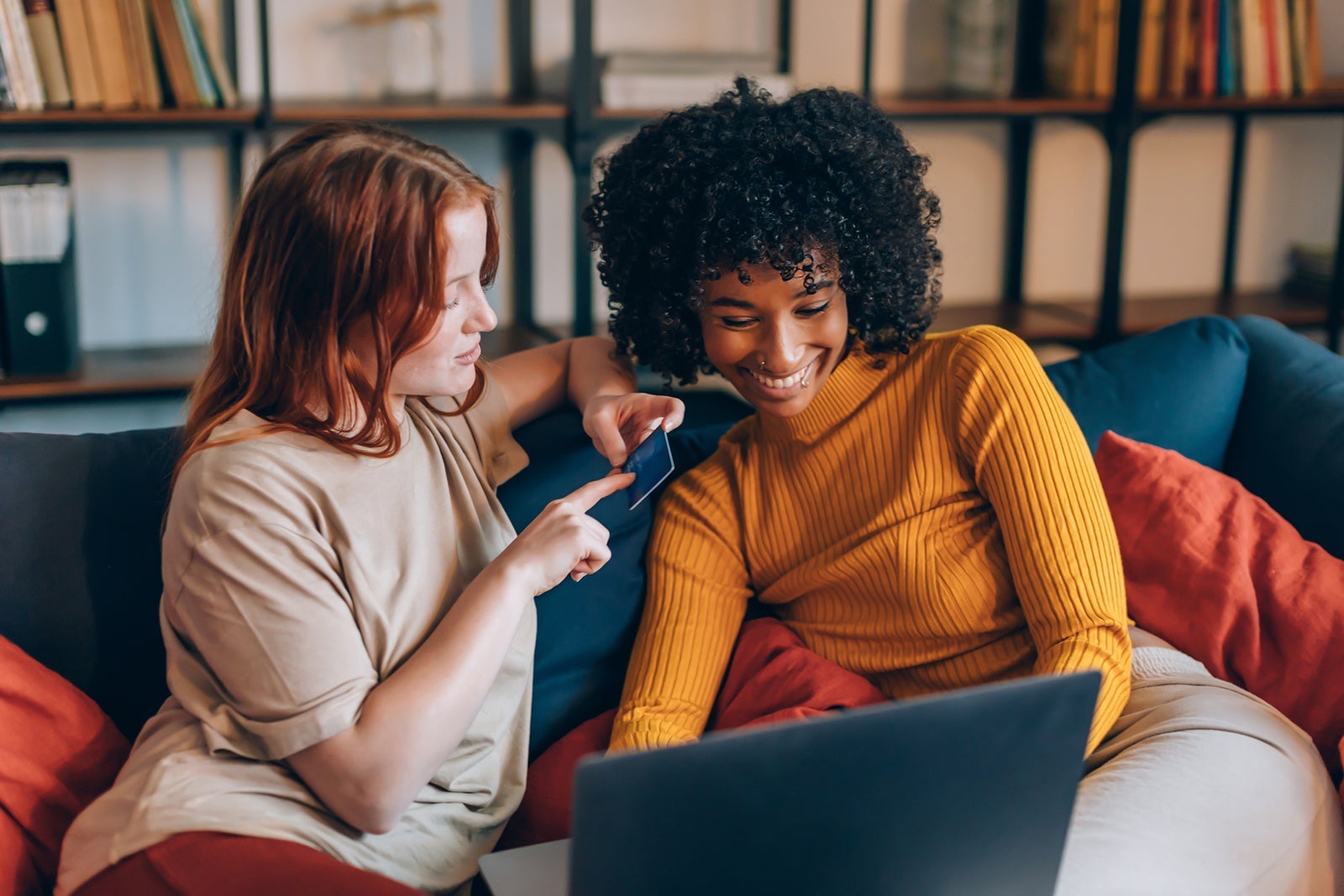 Two Cheerful Young Women Friends Of Different Ethnicity Using Discount Card And Laptop