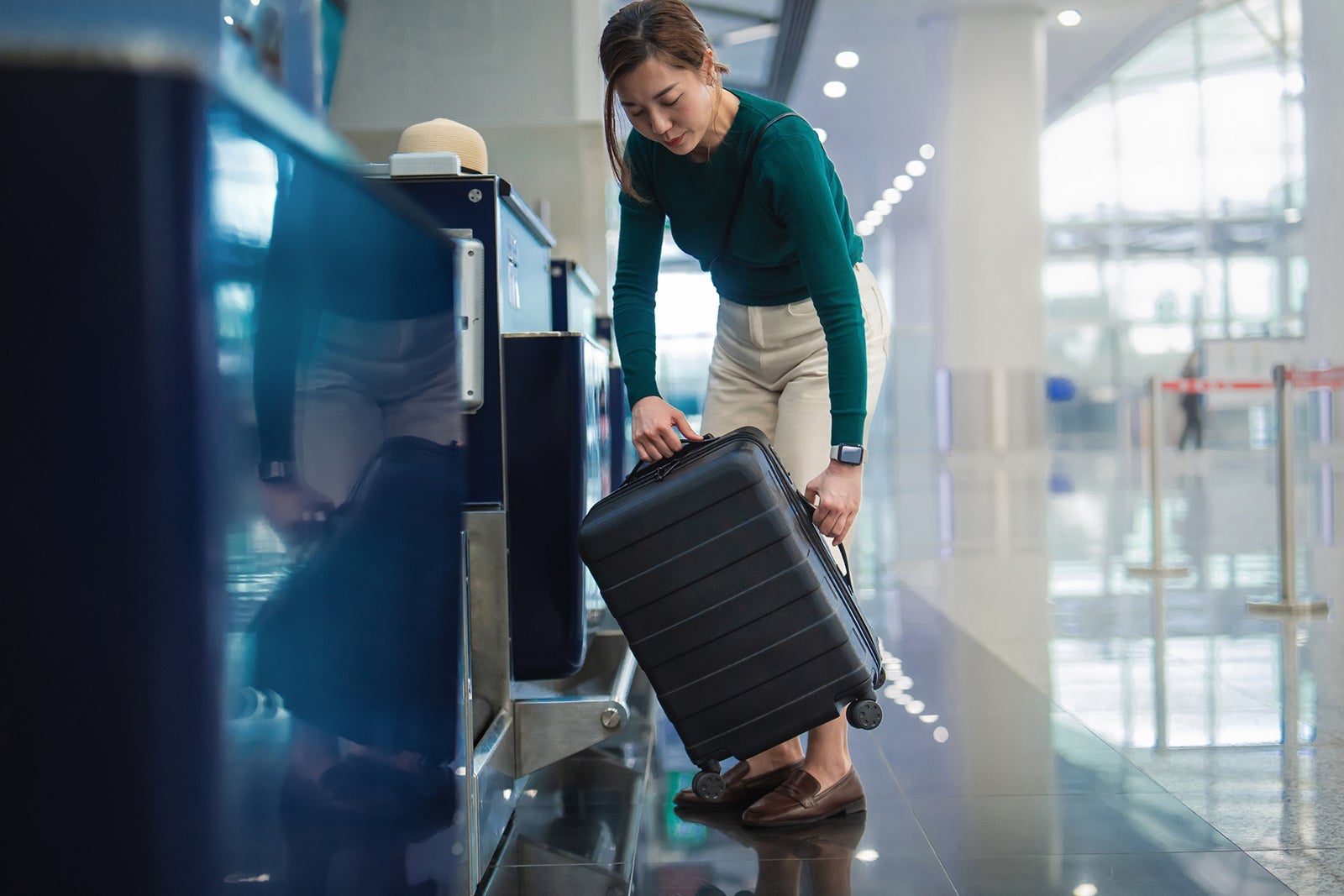 Young Asian female traveller doing luggage check-in at the airline counter in the airport, putting her suitcase on weight scale conveyor belt. Business travel. Travel and vacation concept