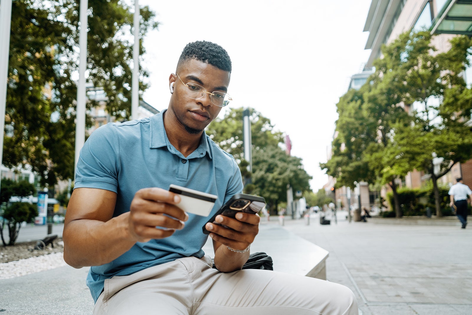 Millennial African American entrepreneur going to work and using smart phone and credit card, man has earphones and listening to music
