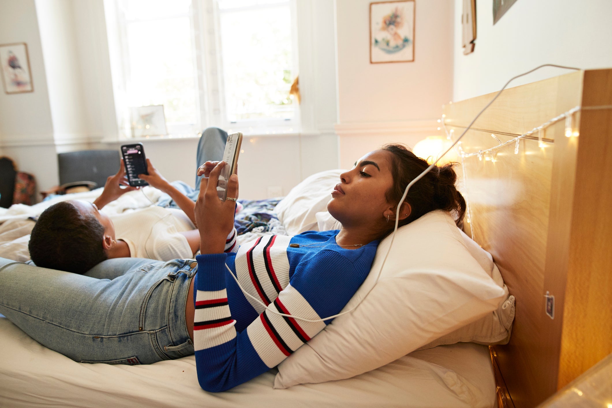 Young female friends using mobile phones in bedroom