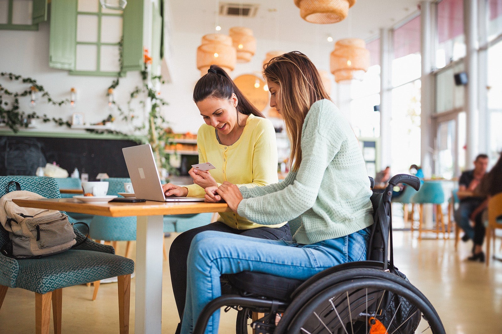 Young disabled woman shopping online in cafe with friend
