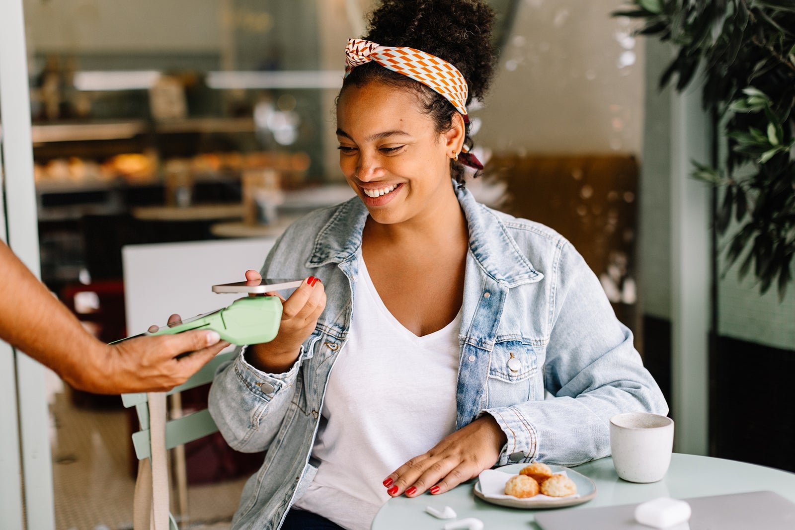 Cheerful woman using NFC with her phone to make a payment at cafe