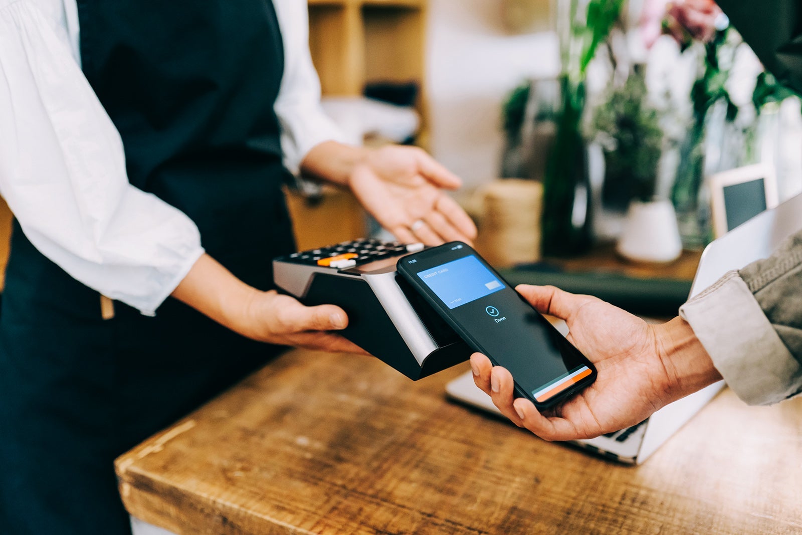 Close up of young Asian man shopping at the flower shop. He is paying with his smartphone, scan and pay a bill on a card machine making a quick and easy contactless payment. NFC technology, tap and go concept