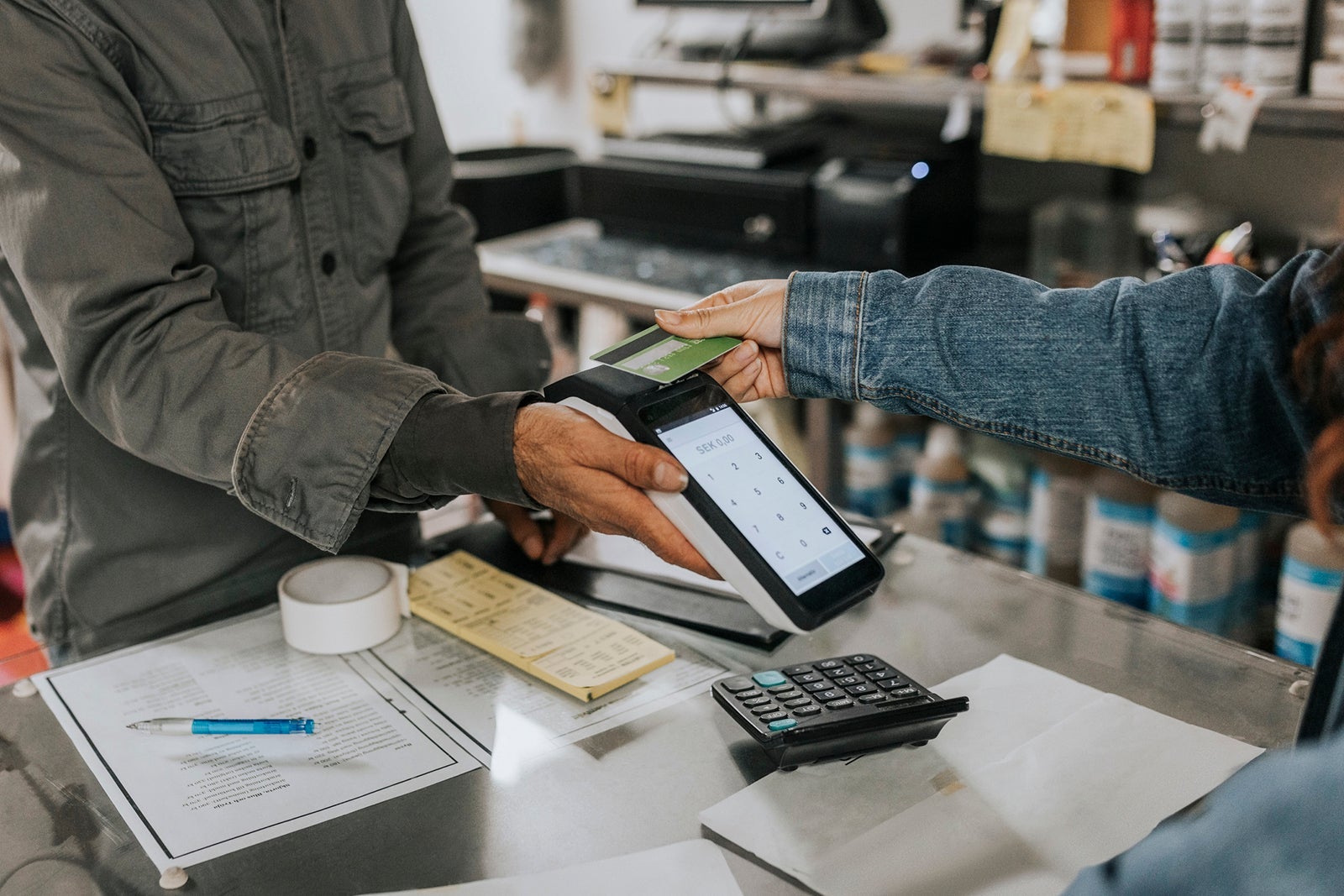 Male tailor holding credit card reader while female client making contactless payment in workshop