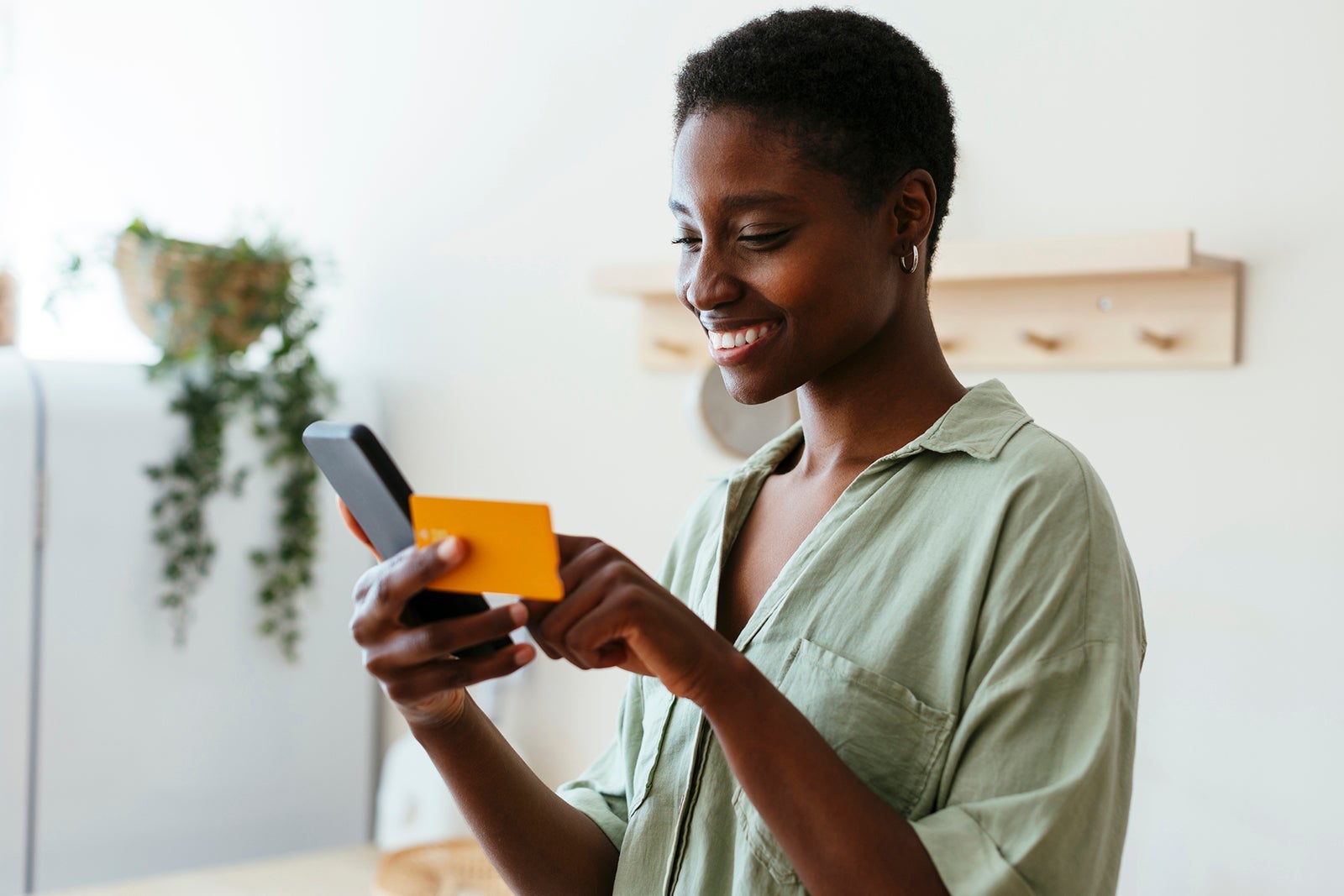 Happy woman making payment through credit card on mobile phone at home