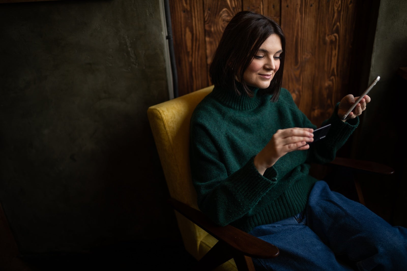 Happy woman shopping online with a credit card and a phone in living room.