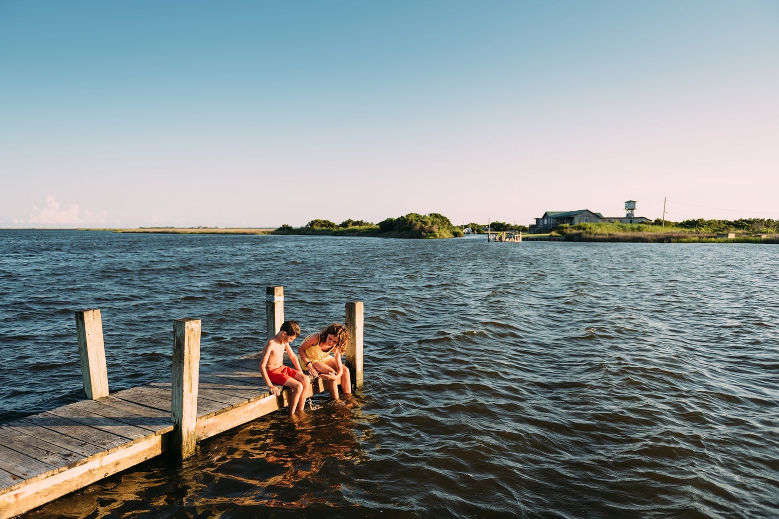 Siblings dipping feet in water on pier