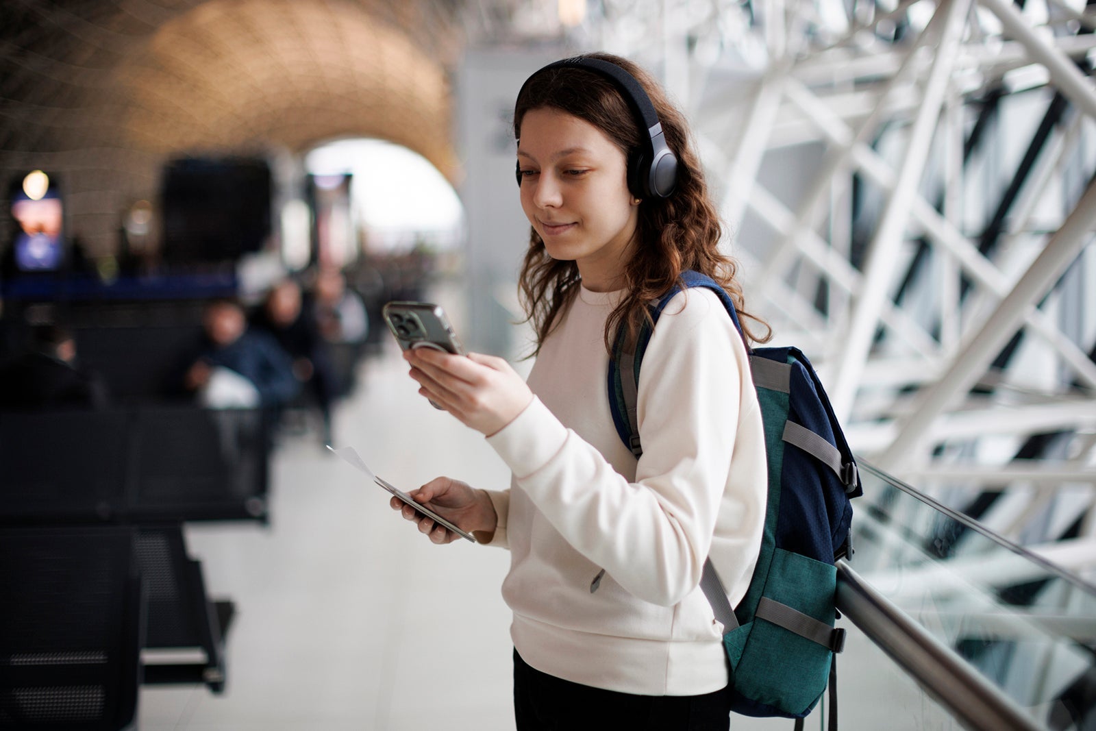 Happy and excited teenage girl with headphones using mobile phone at the airport