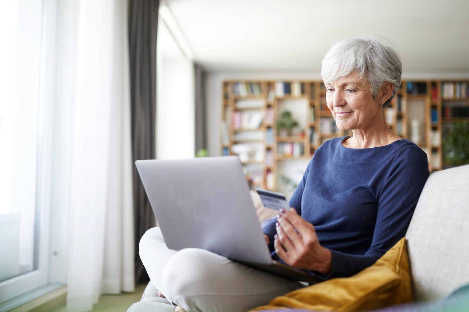 Senior woman using credit card while doing online shopping on laptop at home