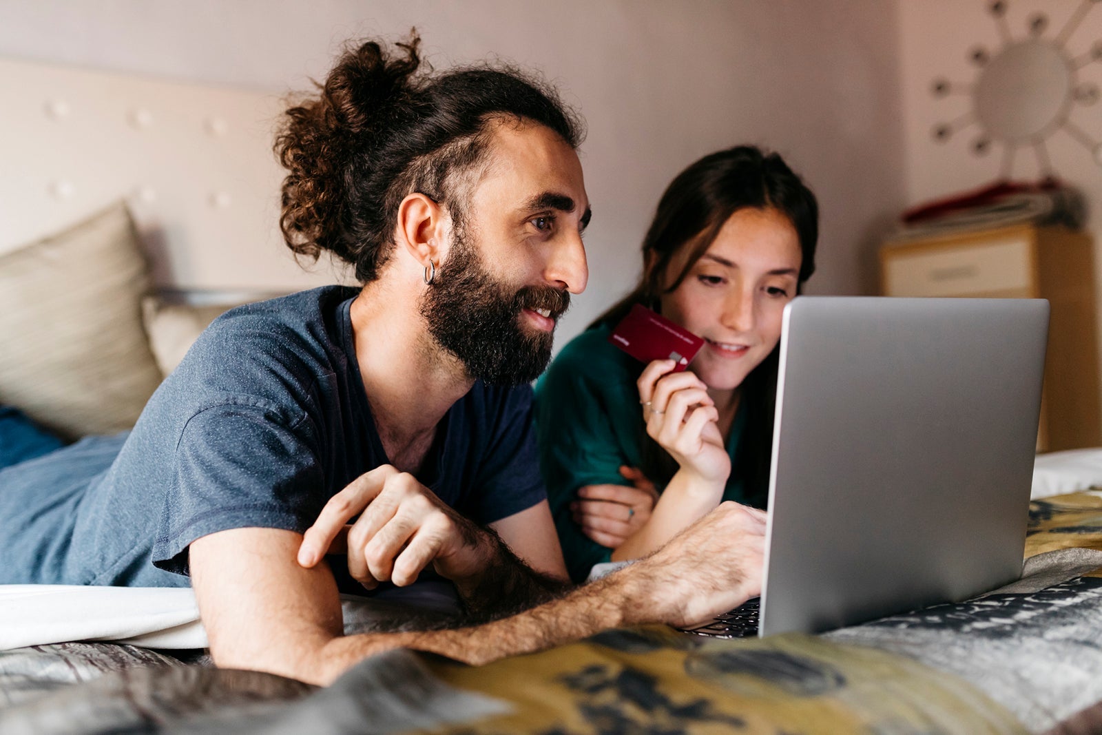 Happy couple lying on bed shopping online