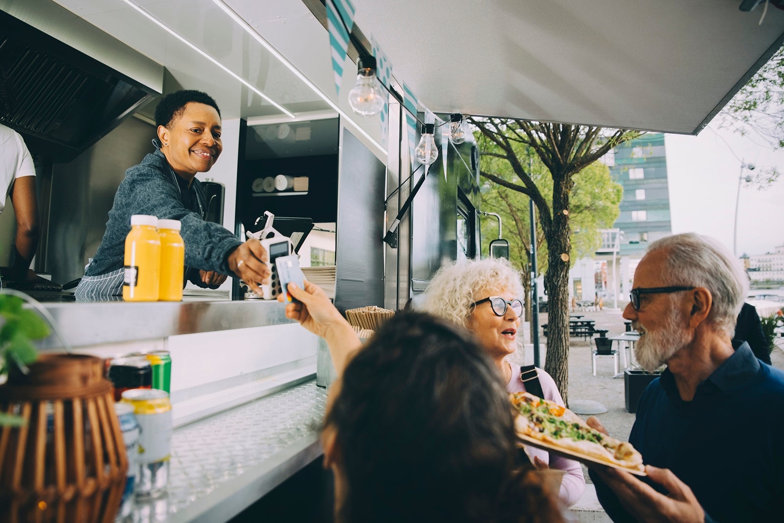 Smiling owner giving credit card reader to customer for payment while standing in food truck