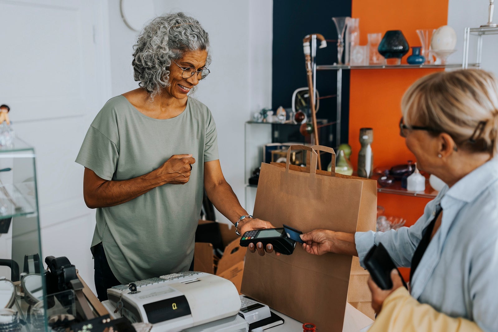 Senior female customer paying through credit card to saleswoman at checkout of antique shop