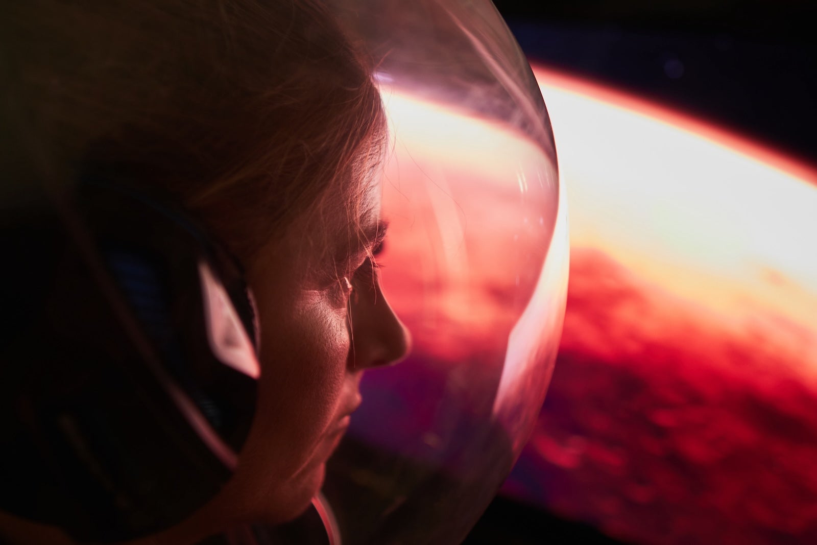 Female astronaut wearing a space helmet and looking to Mars through the space shuttle window. Space journey concept.