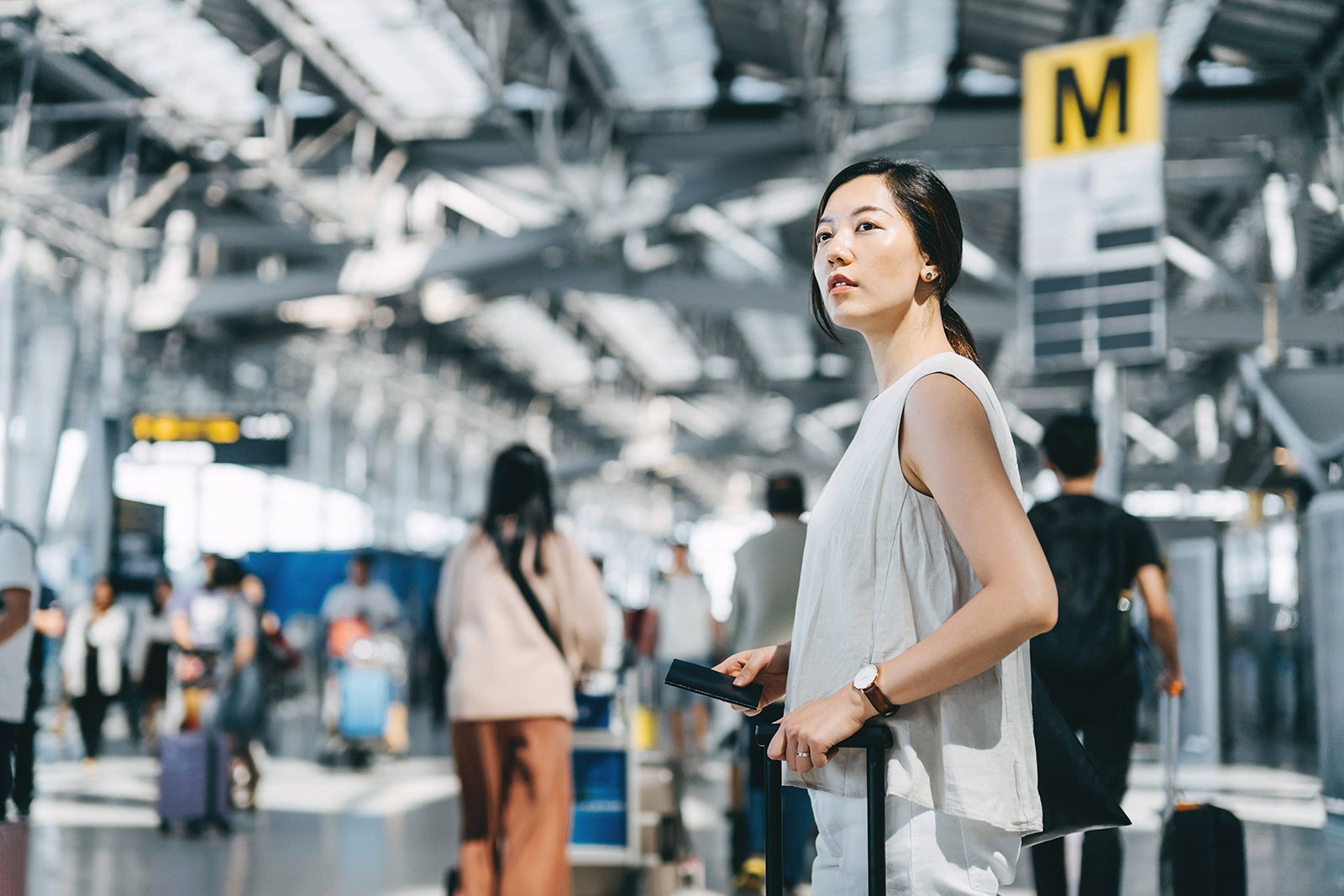 Young Asian woman traveller holding passport and suitcase walking in the international airport hall
