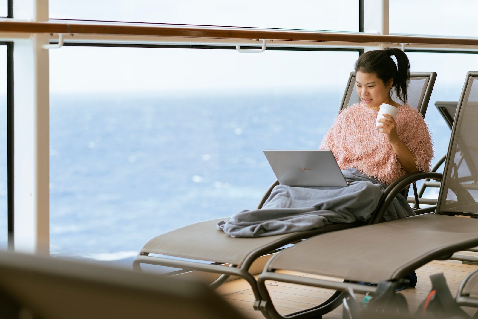 relax chill asian female woman casual cloth working on laptop hand hold coffee cup smiling happiness on casual bench with ocean background