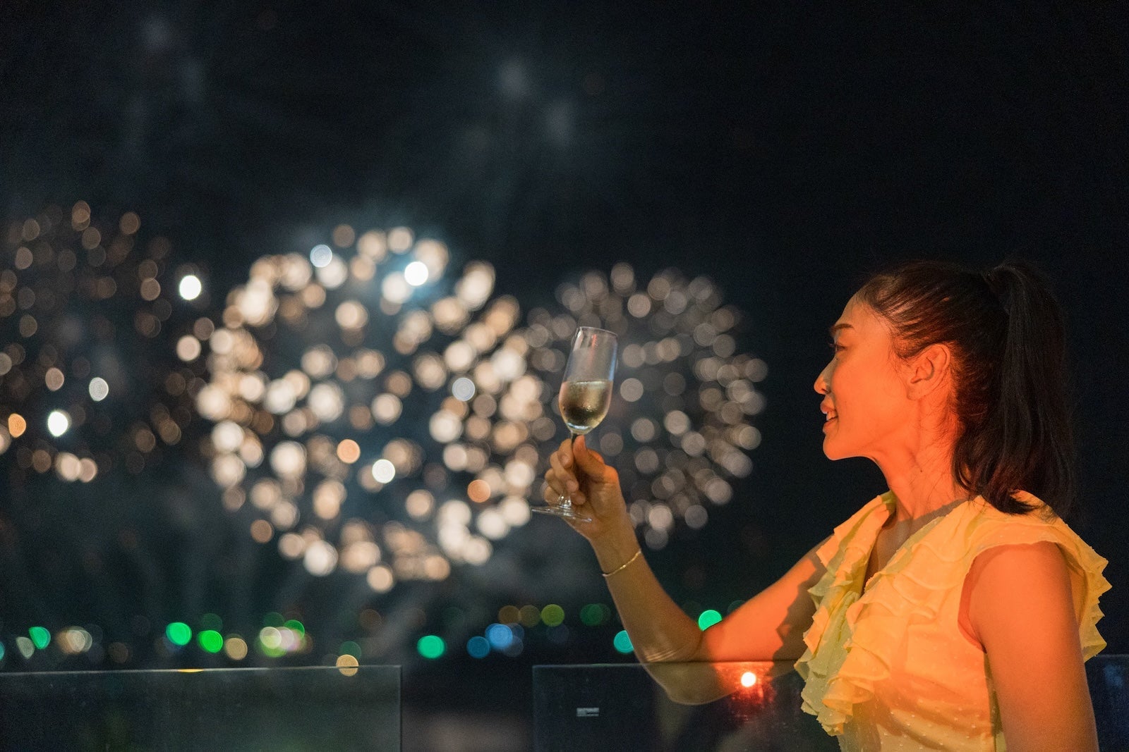 Asian Female enjoy watching firework festival from balcony and a glass of wine in the luxury room in the hotel.