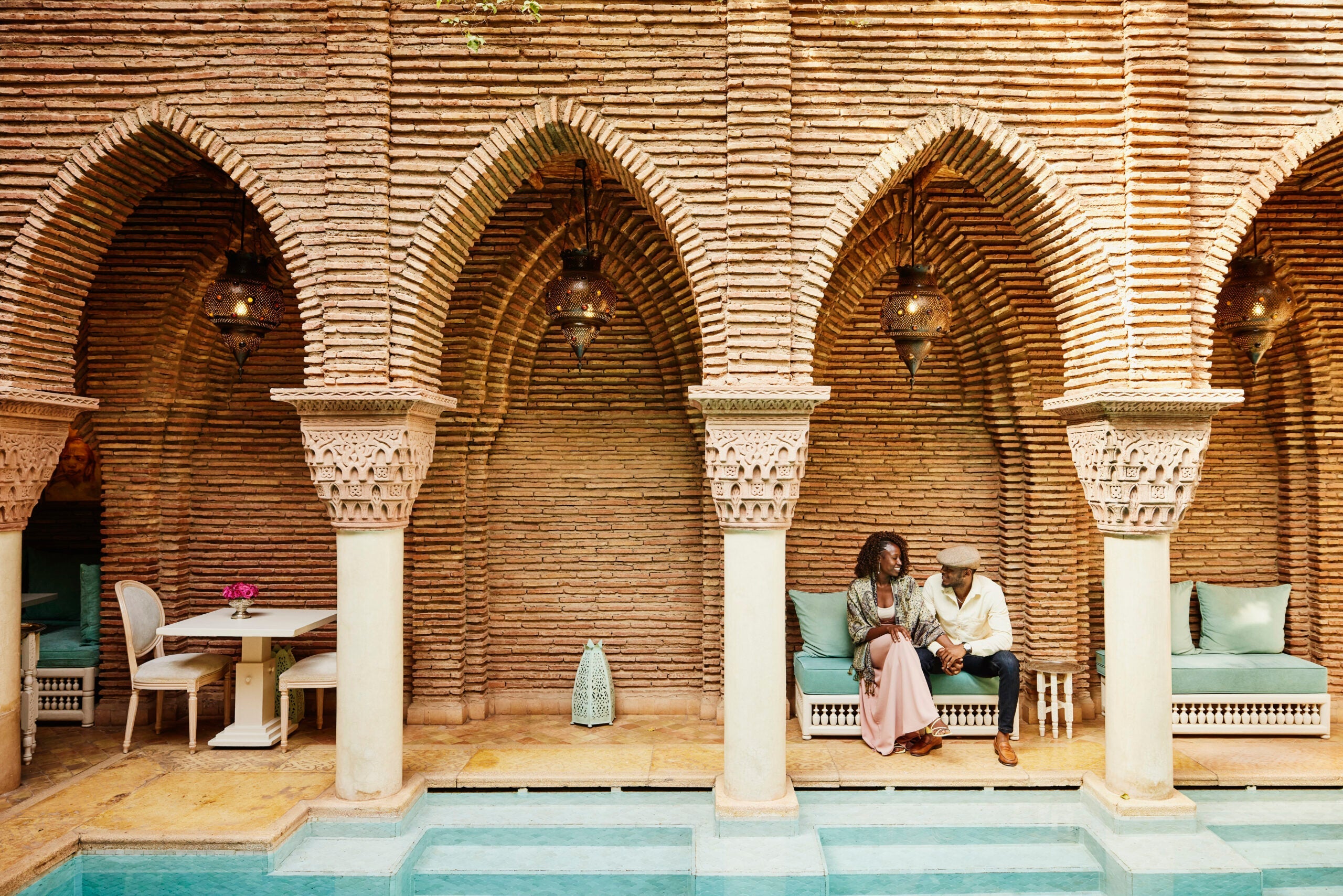 Wide shot of couple holding hands while sitting in courtyard of luxury hotel