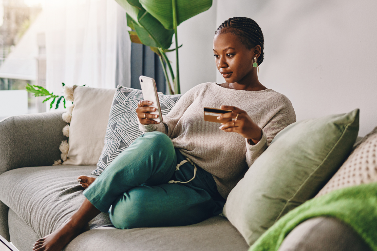 20241016_Credit Card Legislation Sponsored Article_Person using smart phone while holding credit card while relaxing on couch at home