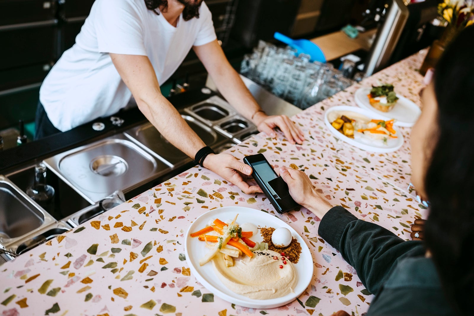 Midsection of owner holding credit card reader for customer doing contactless payment at checkout in restaurant