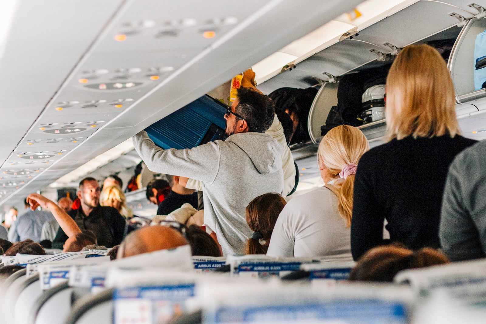 Boarding a plane. Passengers stack baggage on luggage racks.