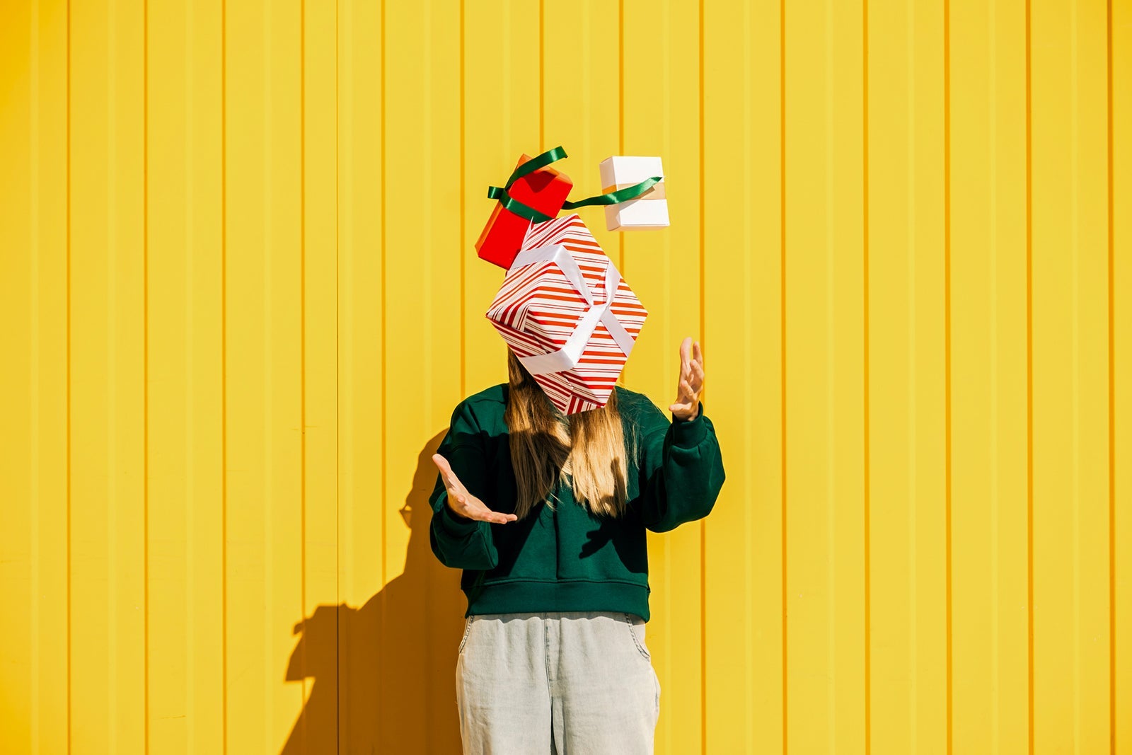 Woman in Christmas hat and green sweater catching Christmas gift box against the yellow wall. Funny summer Christmas and sales concept.
