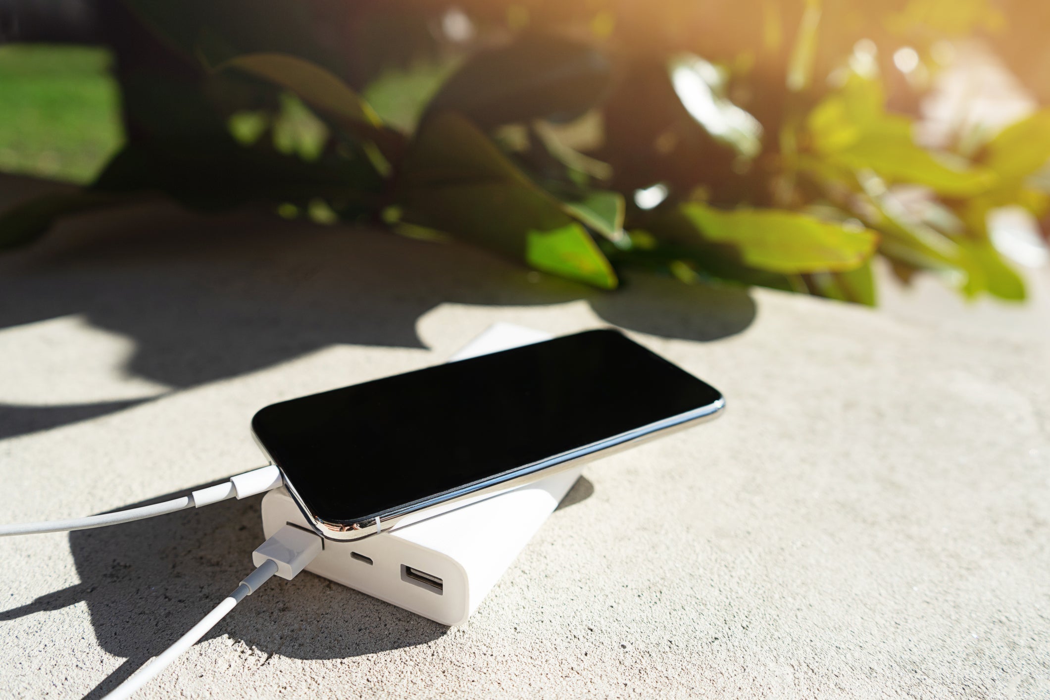 Mobile smart phone charging wirelessly by sharing battery via device on a sunny day on a background of green leaves.