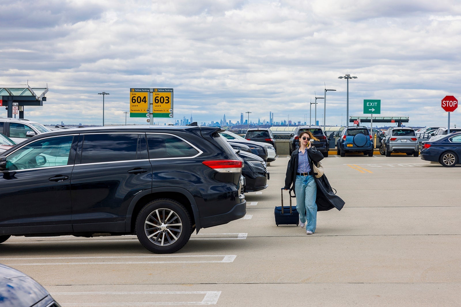 Looking for a car on a parking lot. Busy parking lot with businesswoman on phone, carrying her wheeled luggage to airport