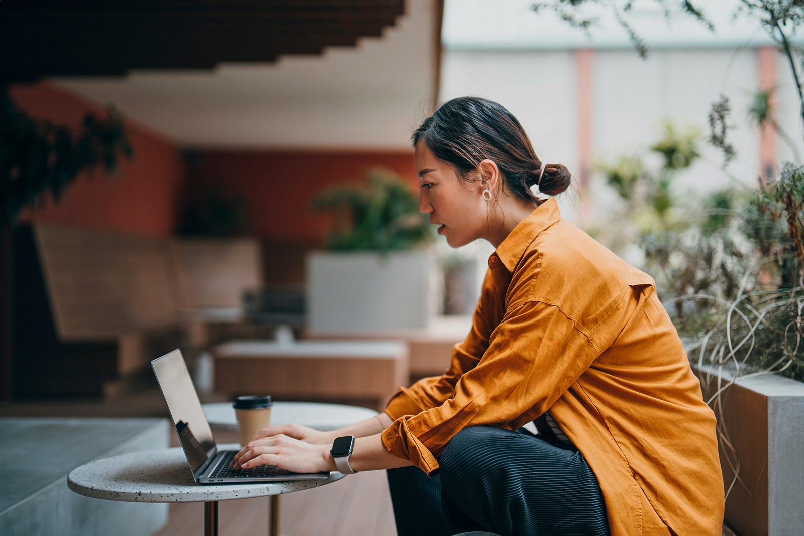Confident young Asian businesswoman working on laptop with business clients in outdoors co-working space, surrounded by green plants. Remote working. Working outdoors with technology. Staying connected to her business. Lifestyle. Business or leisure theme