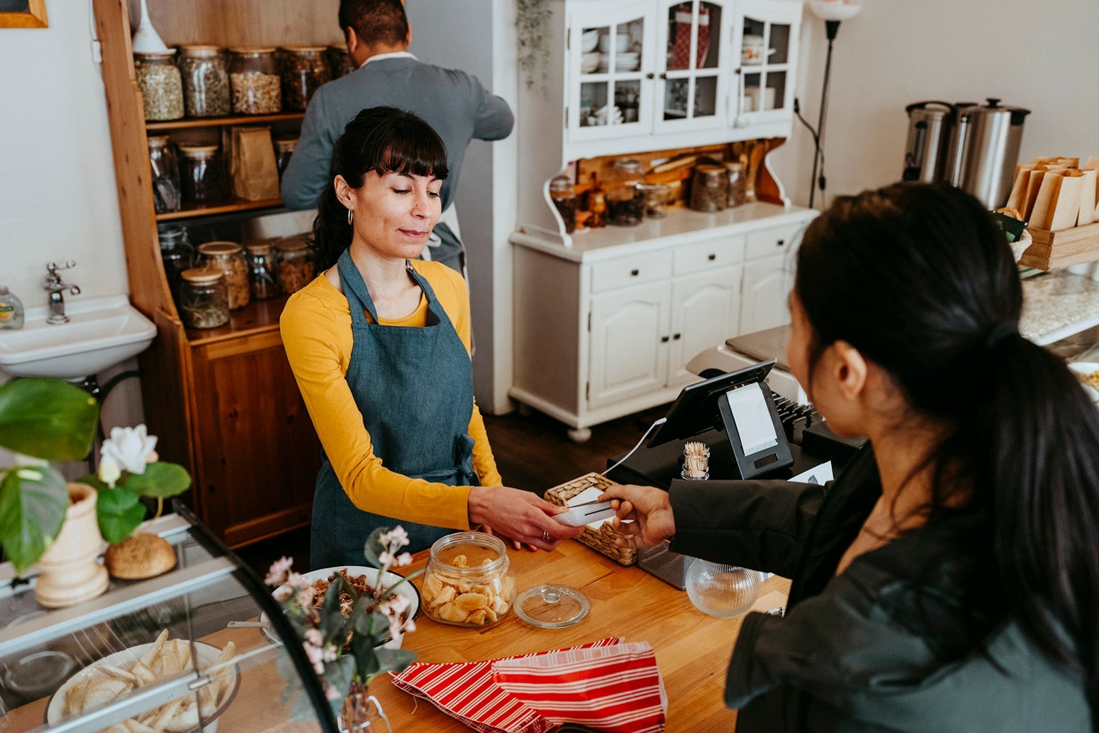 Female barista holding credit card reader for customer paying at checkout in deli