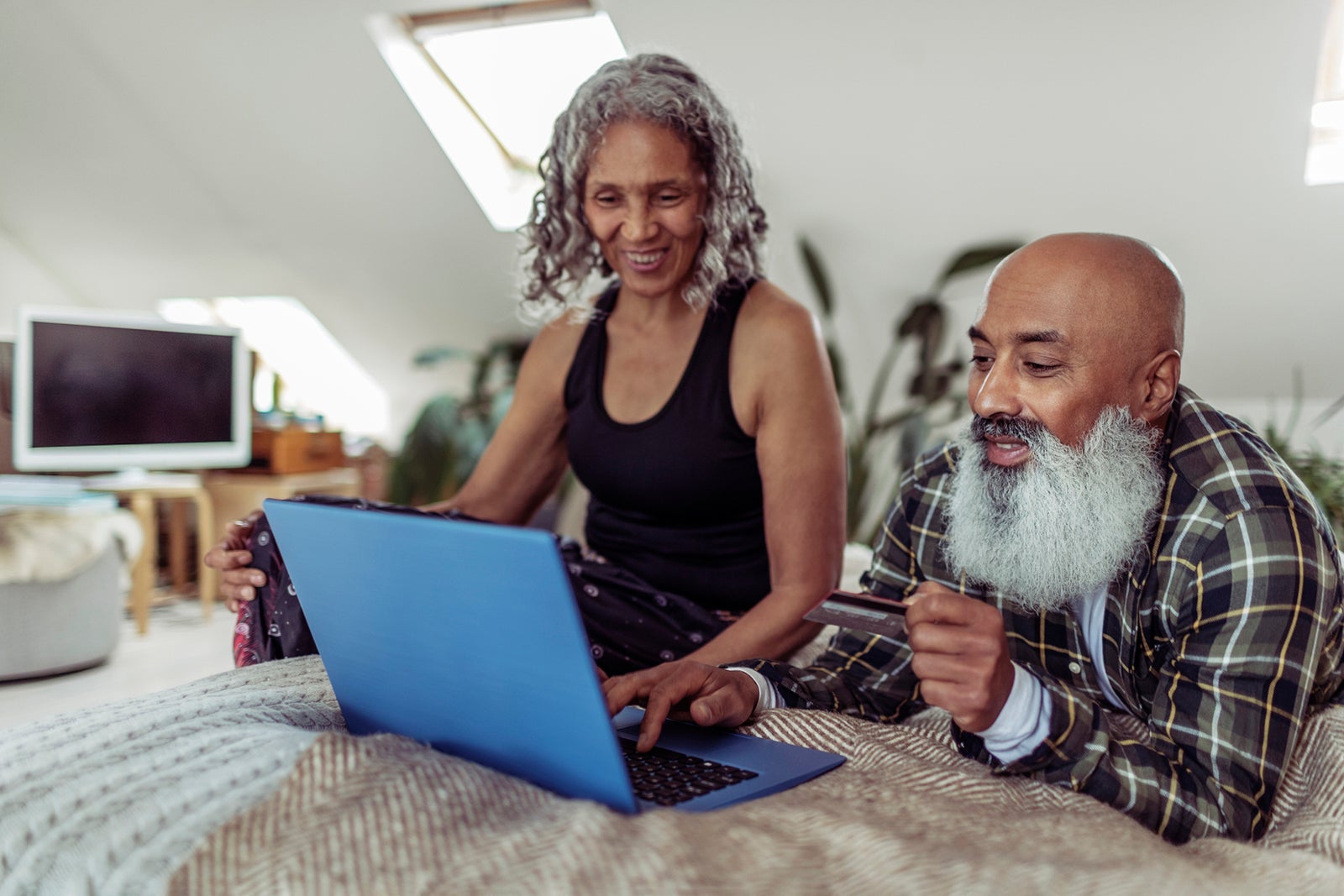 Happy senior couple with credit card using laptop on bed