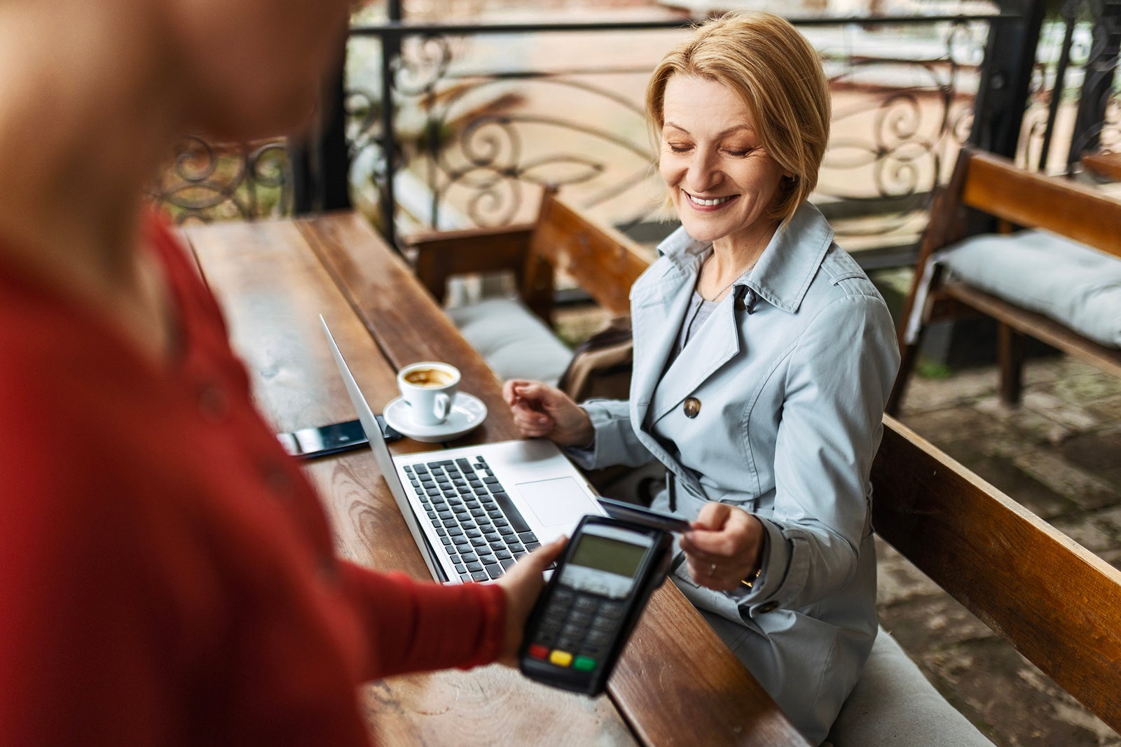 Mid adult businesswoman working with a laptop in a coffee shop paying with credit card