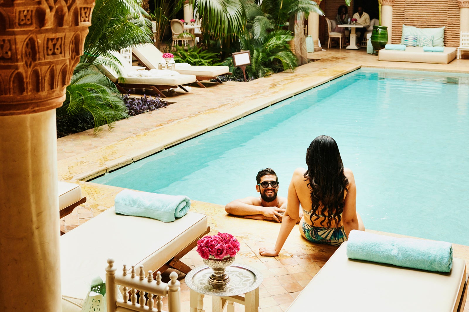 Wide shot of couple relaxing at edge of pool in at luxury hotel